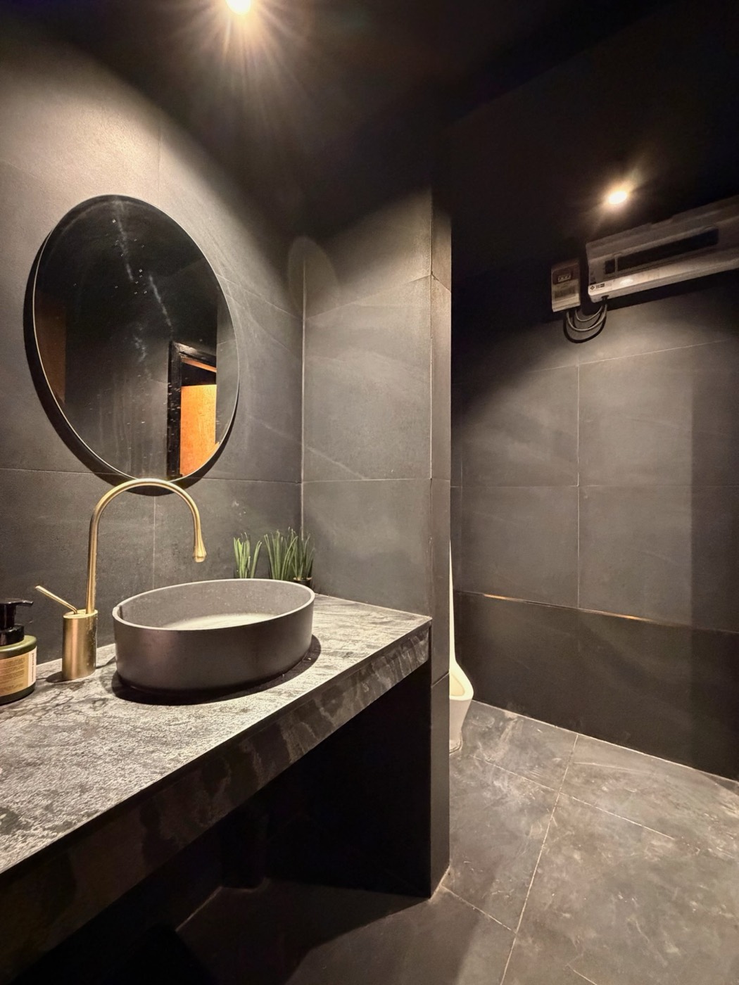 A bathroom in dark stone with a brass tap