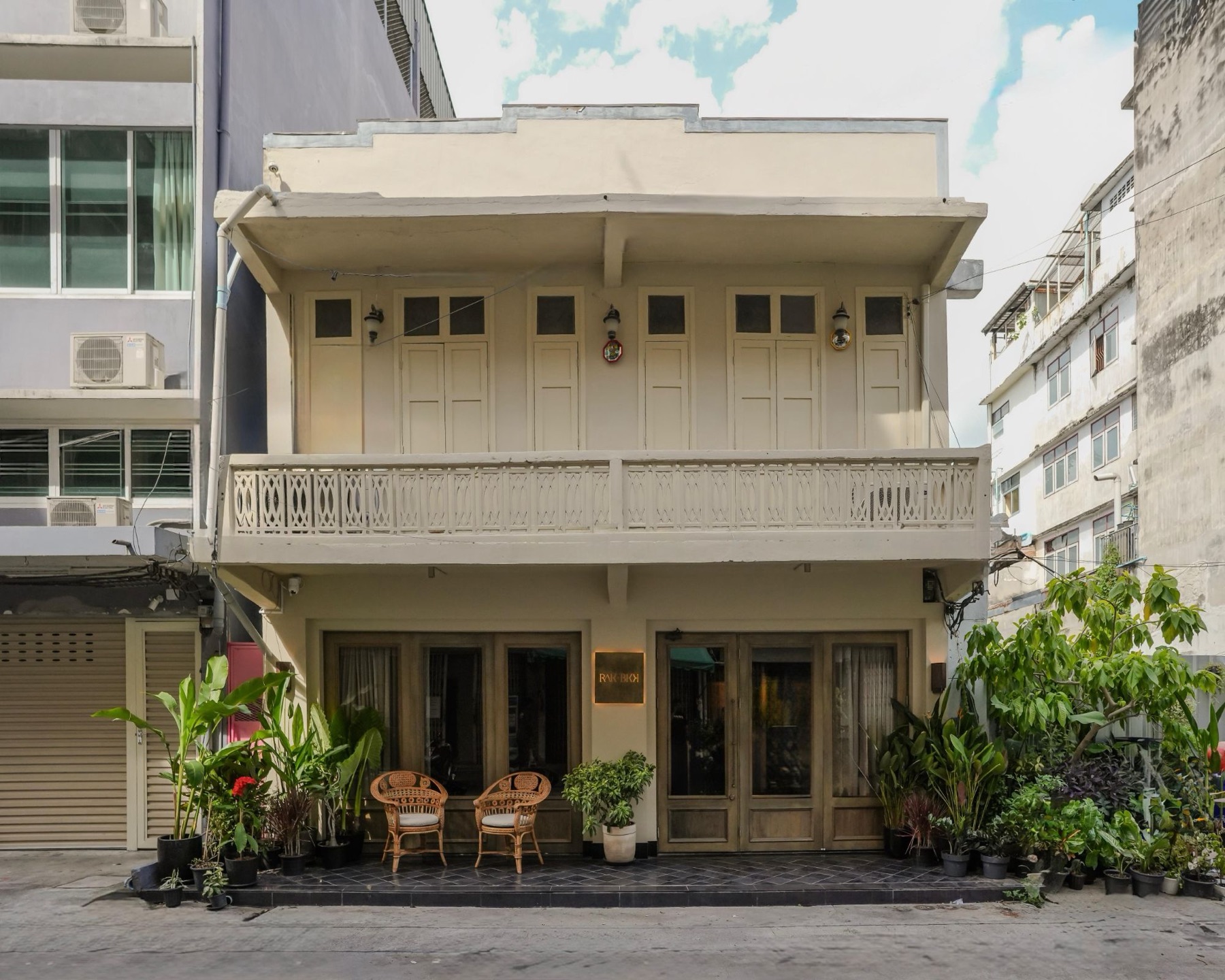 The front of RAK BKK, a restored shophouse with timber doors and plants