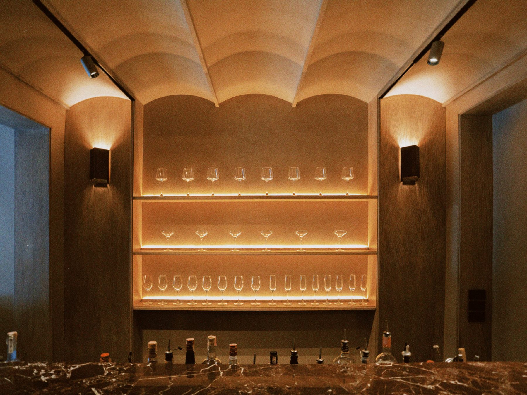 The long bar under a vaulted plaster ceiling, glasses lit on the shelves