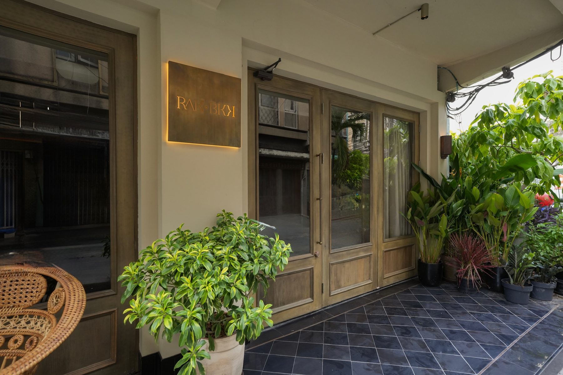The entrance to RAK BKK with its brass sign, timber doors and plants