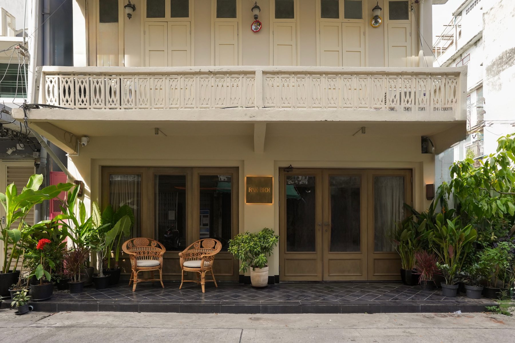 The front of RAK BKK: a restored two-storey shophouse with timber doors, rattan chairs and plants